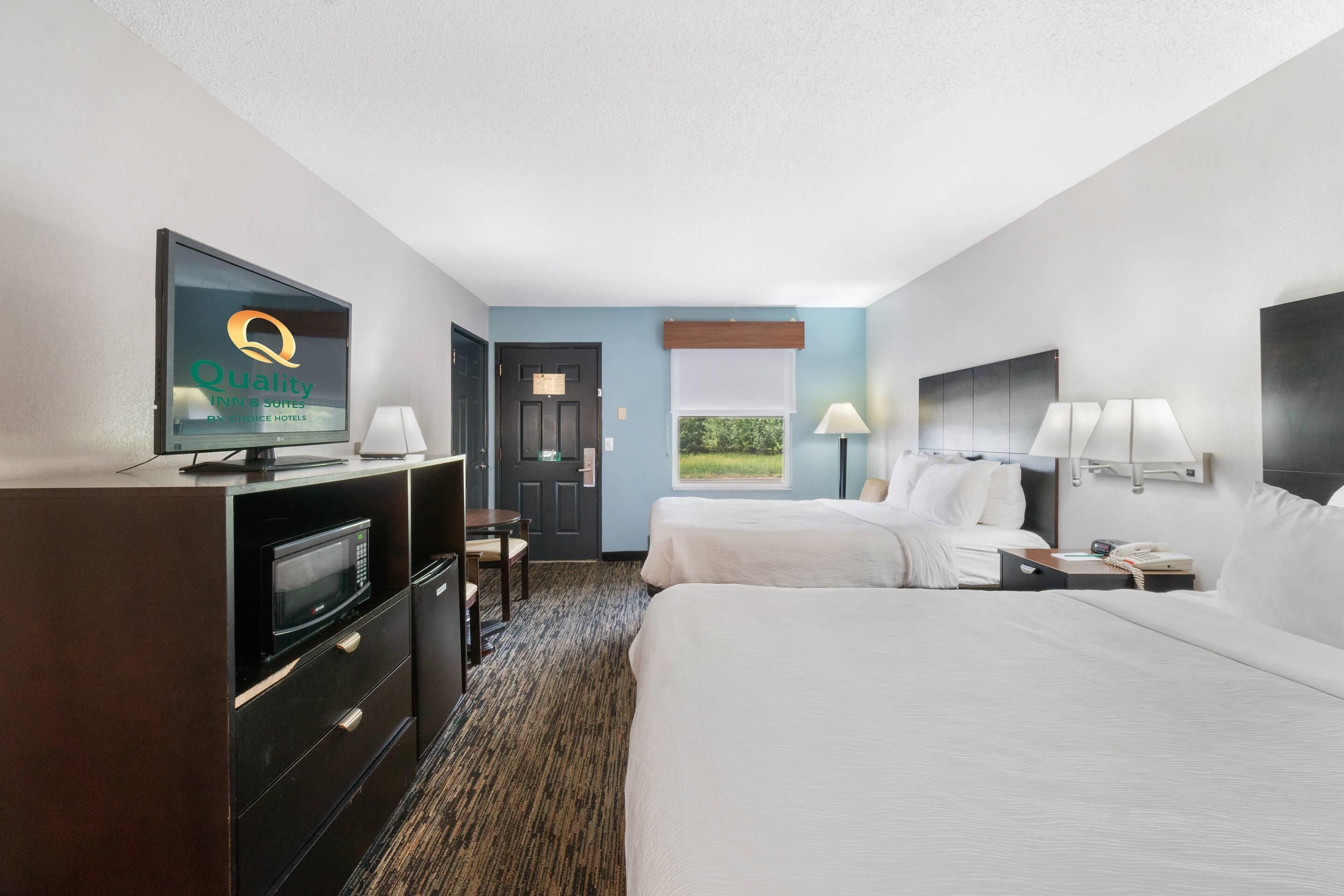 A hotel room with a television, two beds, a desk, a chair, a window with a view, and a door.