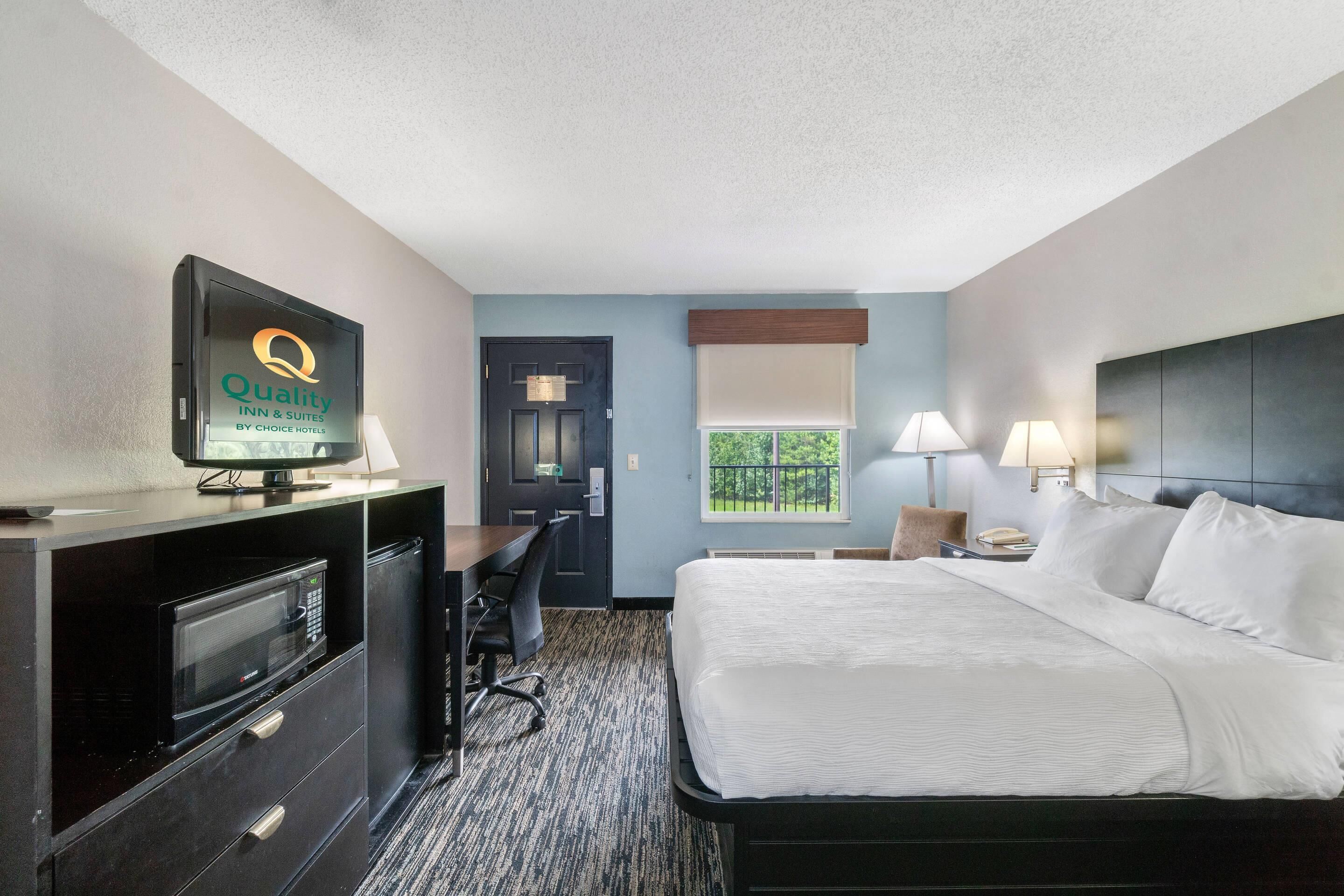 A hotel room with a bed, desk, chair, television, and a window with a view.