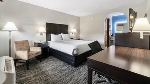 A hotel room with a bed, a chair, a desk, a lamp, and a heater.