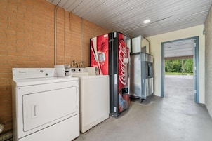 Uma área de lavanderia com uma máquina de lavar Whirlpool, um refrigerador Coca-Cola e um forno de aço inoxidável.