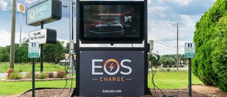 A charging station with a digital screen advertising the EOS app, surrounded by greenery and a Shell sign.