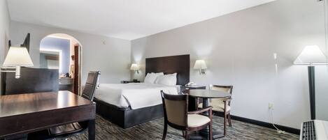 A hotel room with a bed, a desk, a chair, a table, and two lamps.