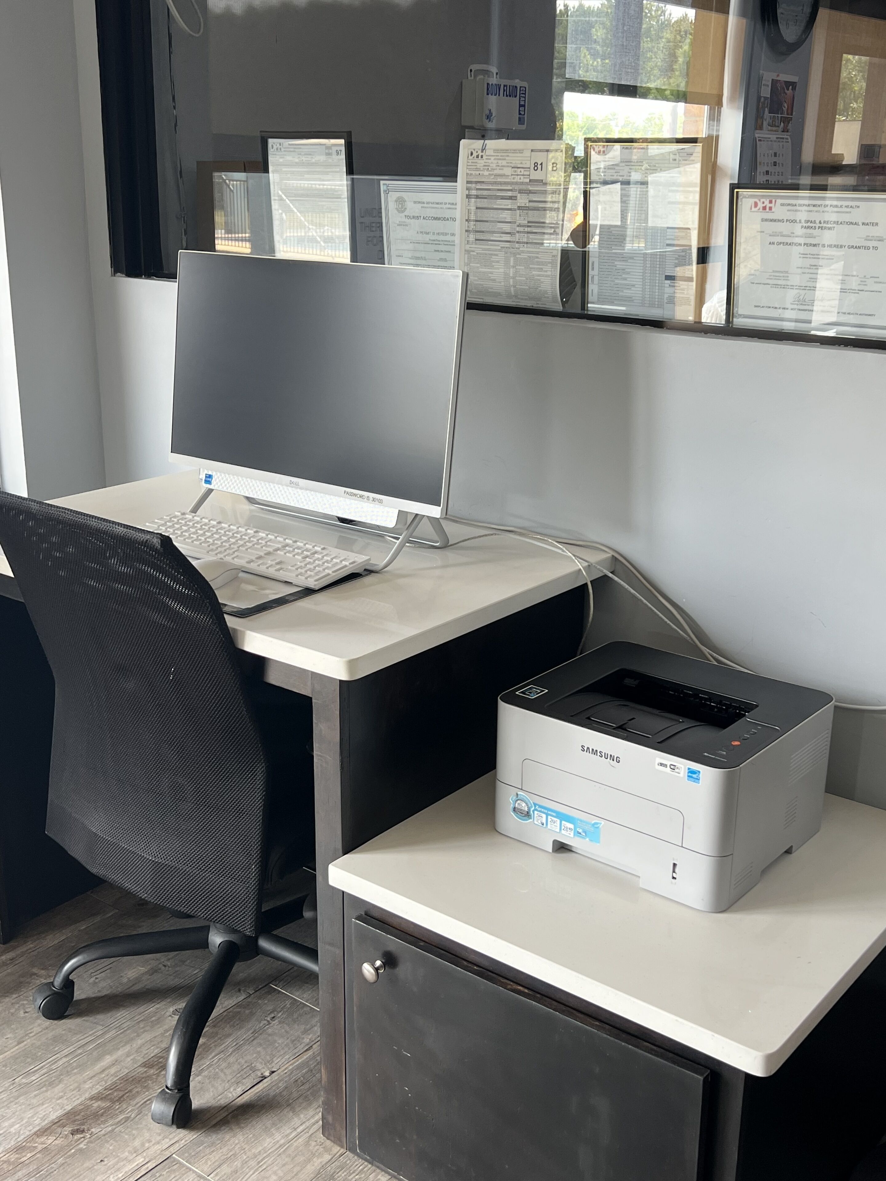 A workspace with a desktop computer, a printer, and documents on the wall.