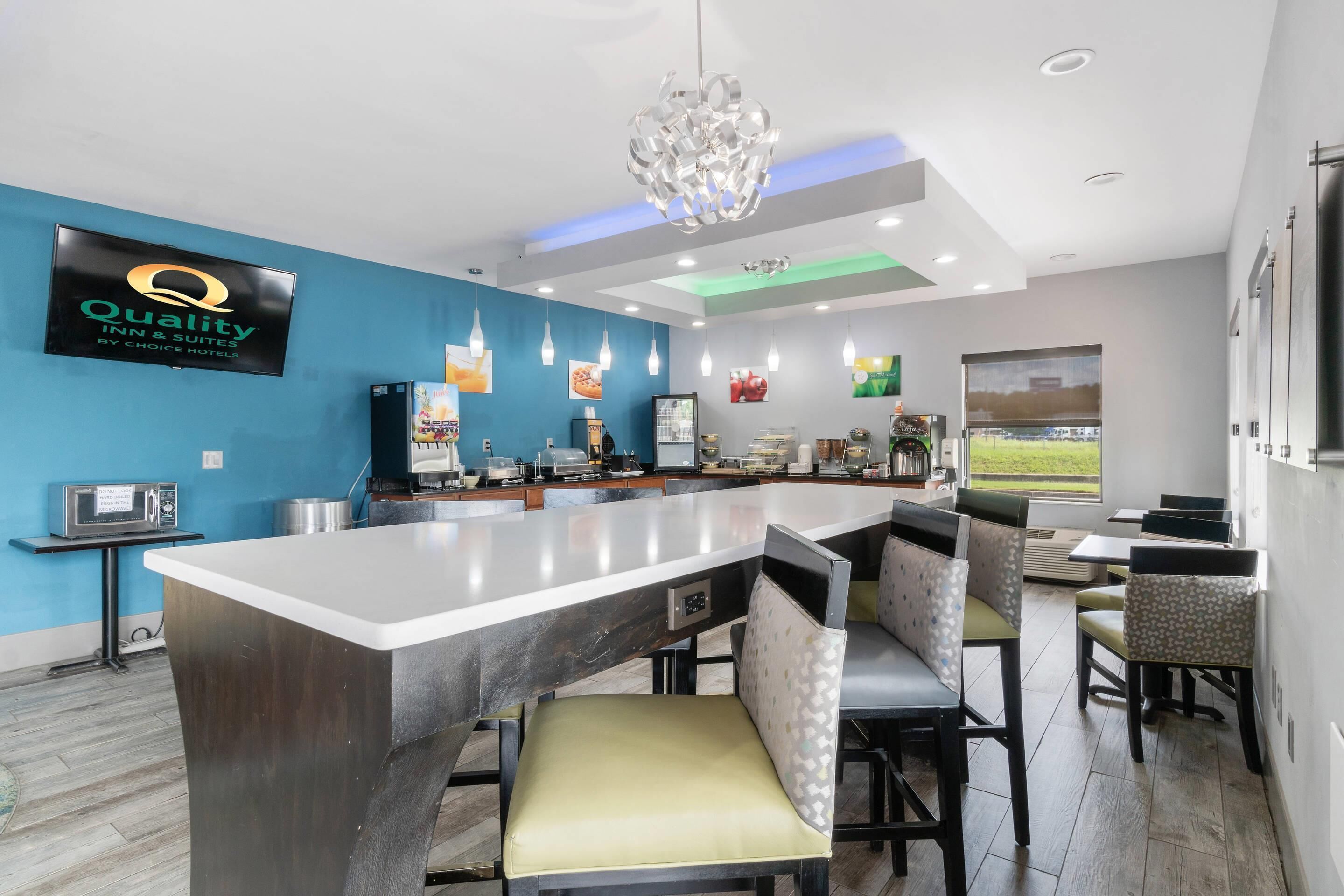 A modern kitchen area with a bar, seating, and a large screen displaying the hotel name.