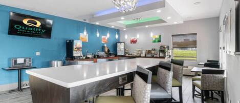 Een moderne keukenhoek met een bar, zitplaatsen en een groot scherm waarop de naam van het hotel staat.