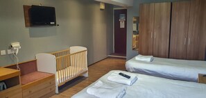 A hotel room with a crib, two beds, a TV, and a wardrobe.
