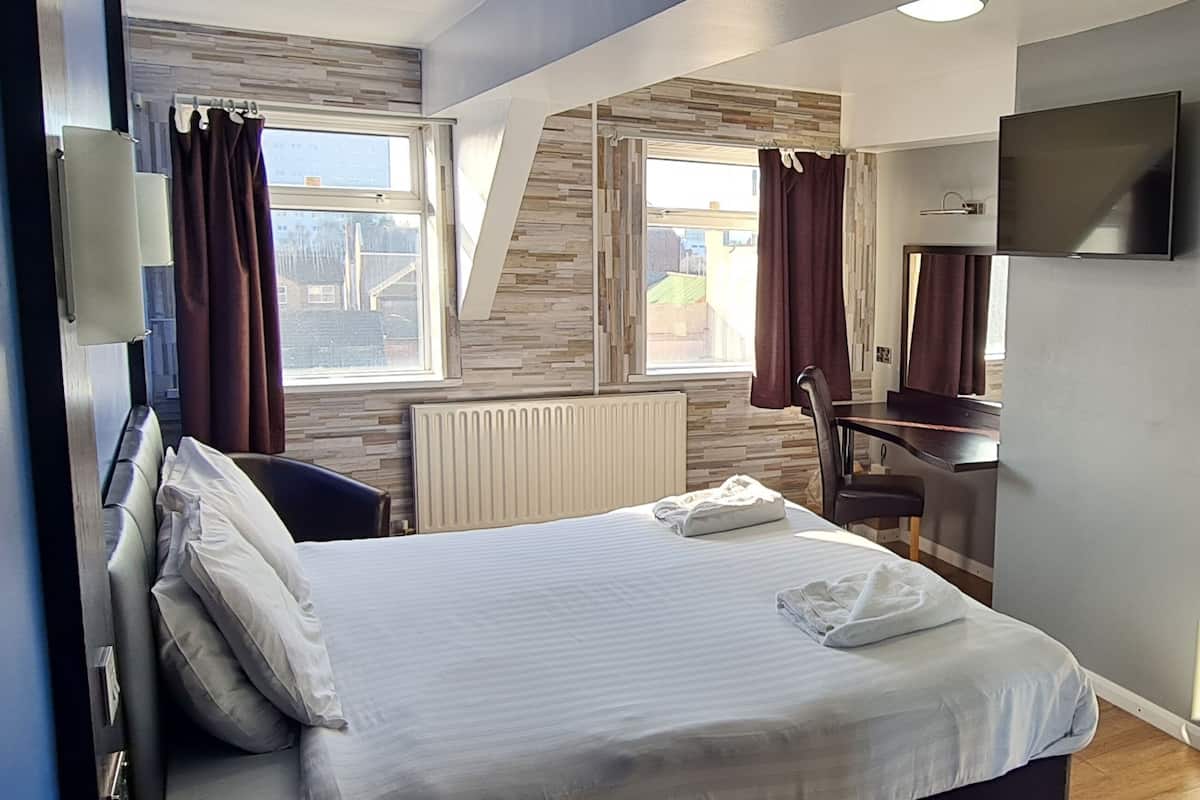A hotel room with a bed, a desk, a chair, a TV, and a window with curtains.