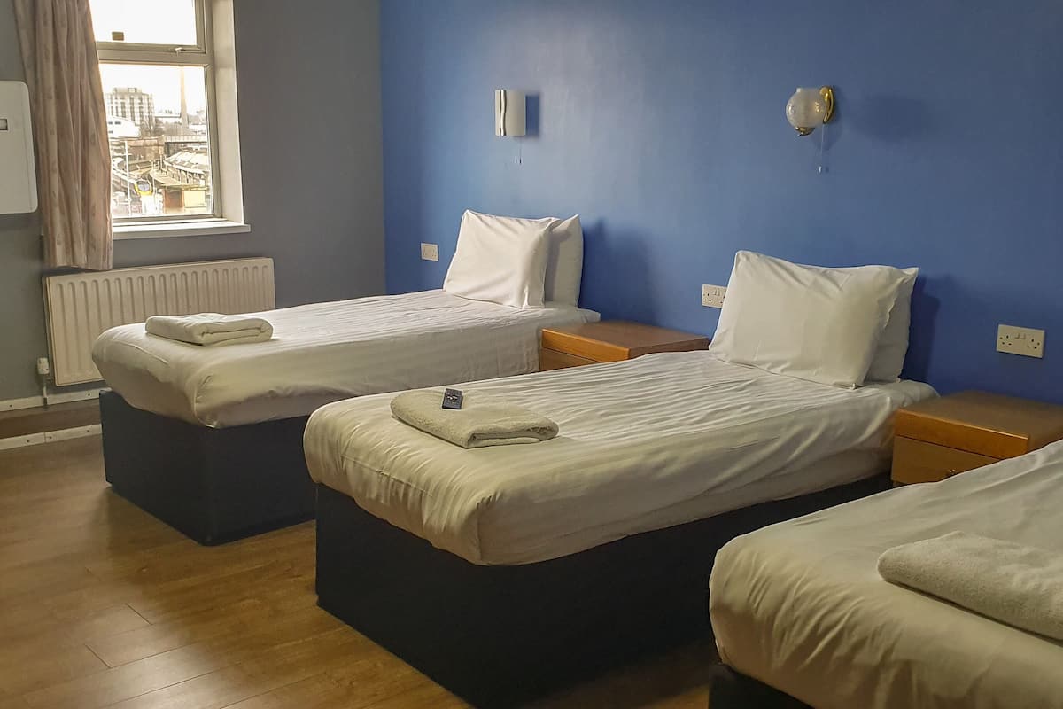 A room with two single beds, a radiator, a window with curtains, and a wall-mounted light fixture.