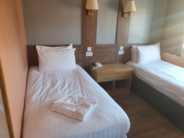 Habitación de hotel con dos camas individuales, una mesita de noche de madera con teléfono y lámparas de pared.