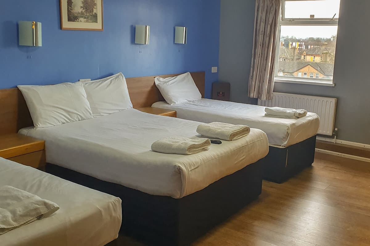 A hotel room with two beds, a wooden floor, and a window with a view of buildings.