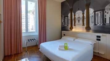 A hotel room with a large bed, a view of a cityscape through the window, and a mural of columns on the wall.