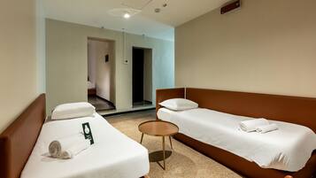 A hotel room with two single beds, a small round table, and a bathroom visible through an open door.