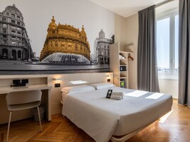 Ein Hotelzimmer mit Bett, Schreibtisch, Stuhl, Kleiderschrank und einem großen Fenster.