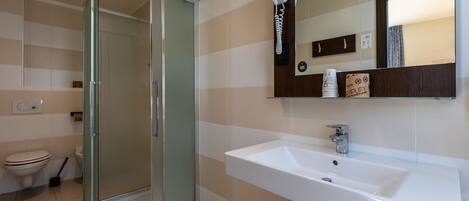 Un baño moderno con cabina de ducha de vidrio, un lavamanos blanco y un espejo con repisa de madera arriba.