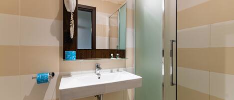A bathroom with a white sink, a hairdryer mounted on the wall, and a glass shower enclosure.