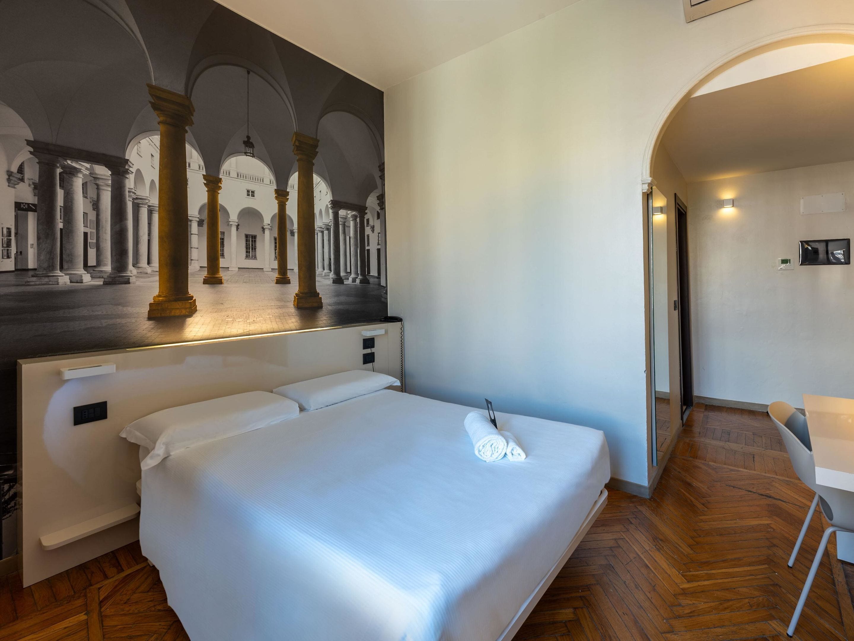 Una habitación de hotel con una cama grande, un escritorio y un mural de un edificio clásico.