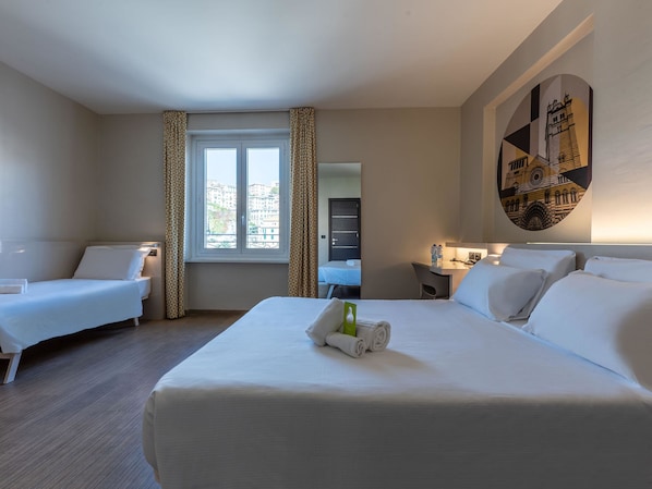Habitación de hotel con dos camas individuales, un escritorio, una silla y un amplio ventanal con cortinas.
