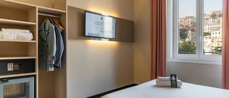 A hotel room with a bed, a wardrobe, a television mounted on the wall, and a window with curtains.
