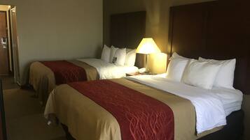 Habitación de hotel con dos camas, cada una con colcha roja y color crema, una lámpara de noche y un teléfono en la mesita.