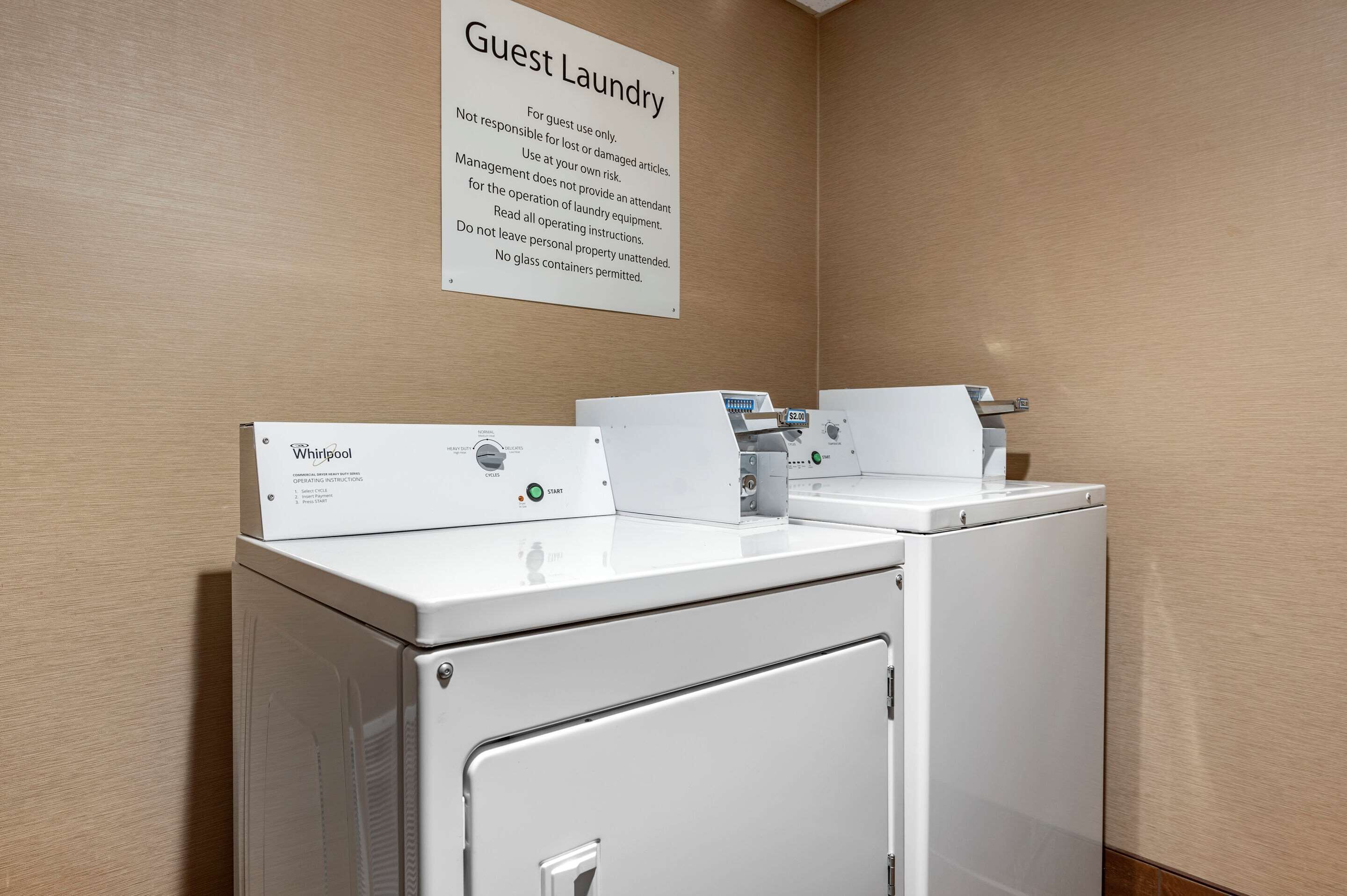 A guest laundry area with Whirlpool washers and dryers, a sign with laundry instructions, and a metal cabinet.