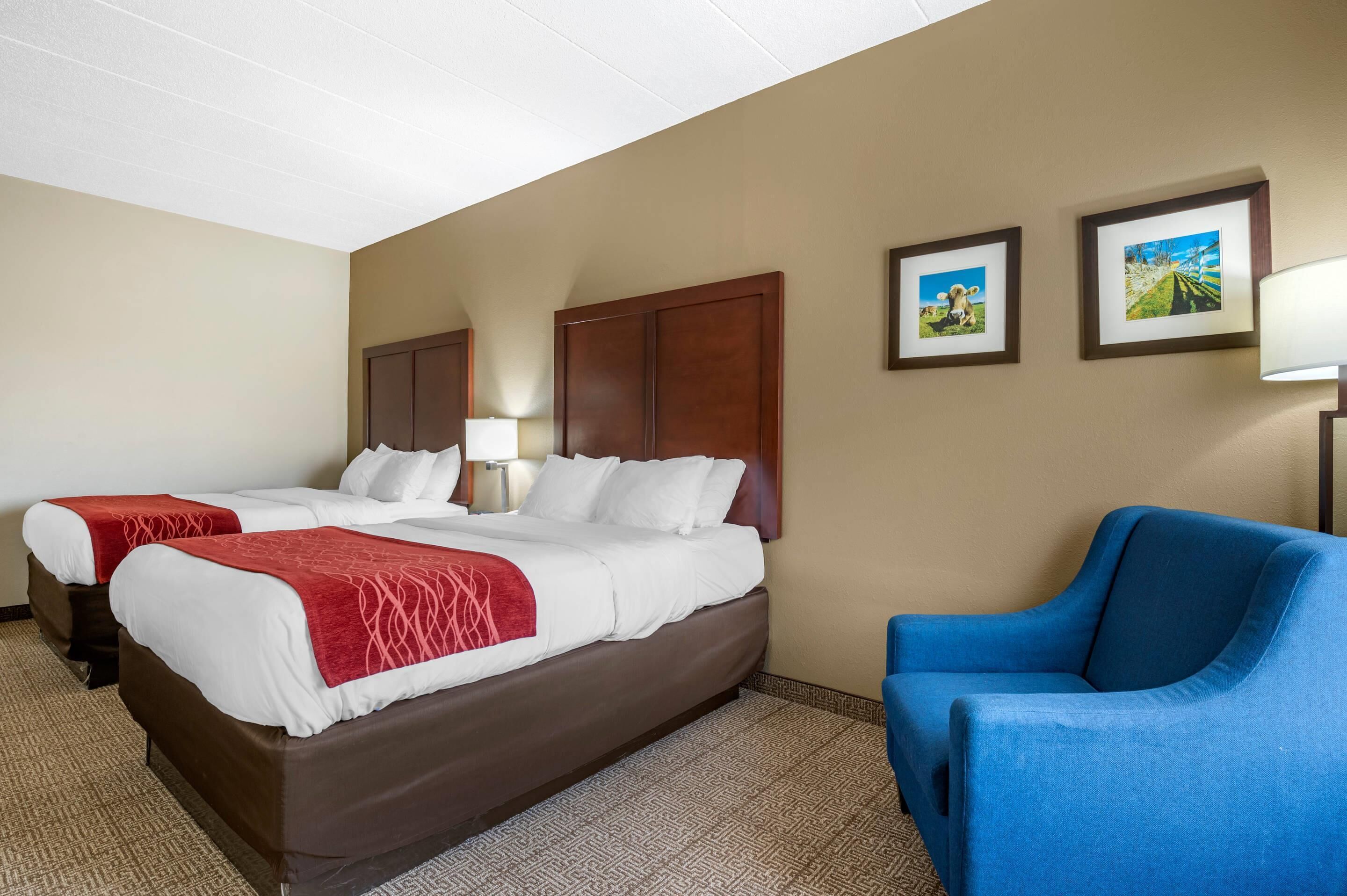 A hotel room with two beds, a blue armchair, and framed pictures on the wall.