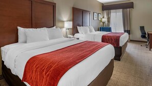Ein Hotelzimmer mit zwei Betten, einem Schreibtisch, einem Stuhl und einem großen Fenster mit Vorhängen.