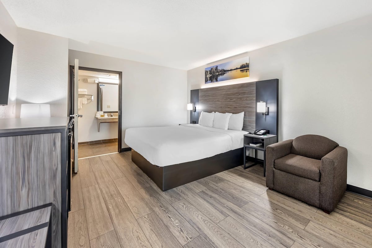 A hotel room with a bed, a chair, a desk, and a nightstand.