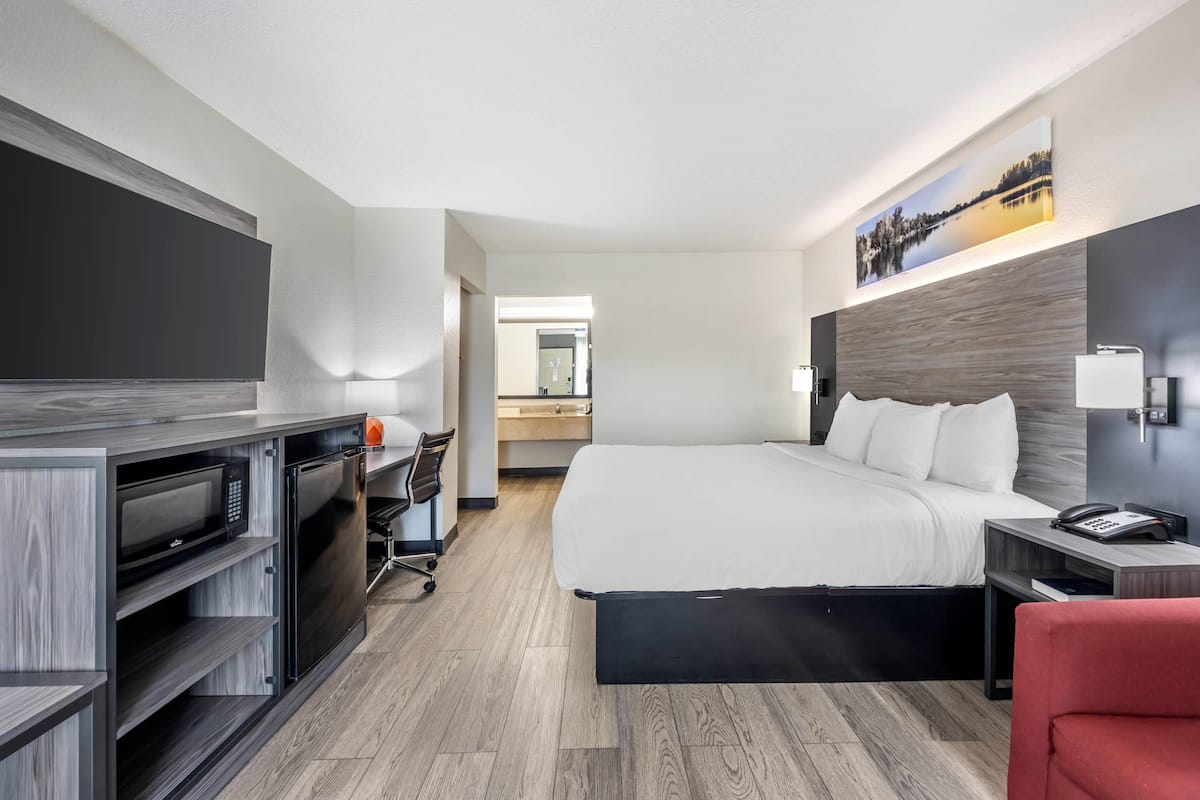 A modern hotel room with a large bed, a desk with a computer, a flat-screen TV, and a microwave.
