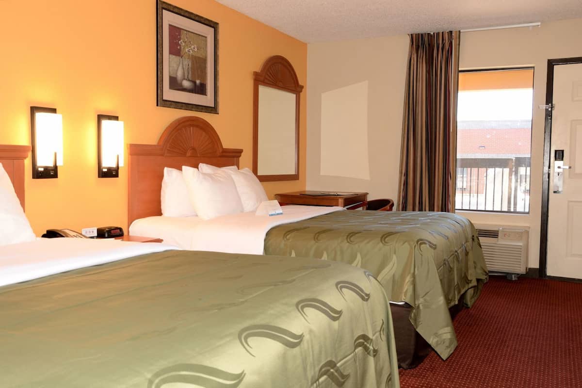 A hotel room with two beds, a desk, a chair, a window with curtains, and a door.
