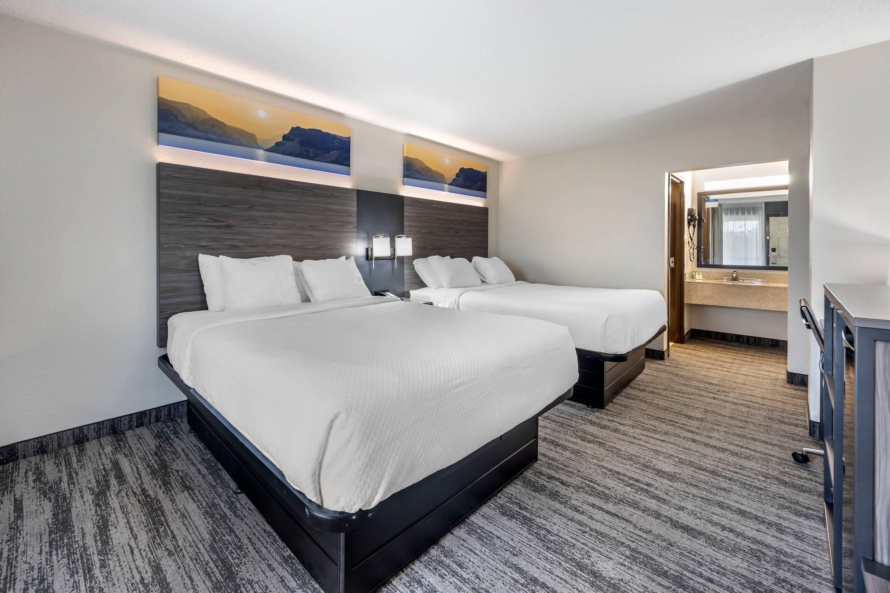 Ein Hotelzimmer mit zwei Betten, einem großen Gemälde an der Wand, einem Schreibtisch mit Spiegel und einem Teppichboden.