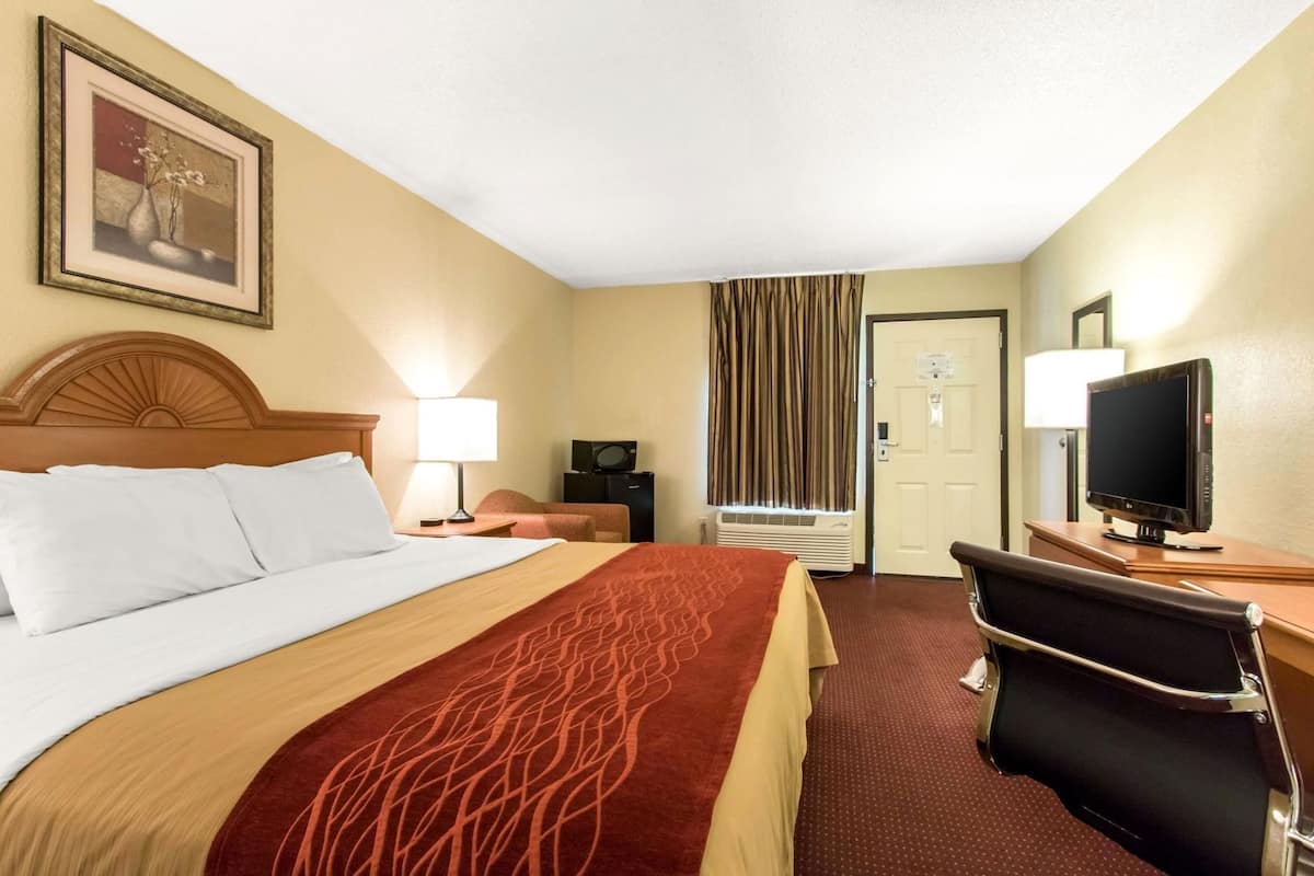 A hotel room with a bed, a desk with a computer, a television, and a window with curtains.