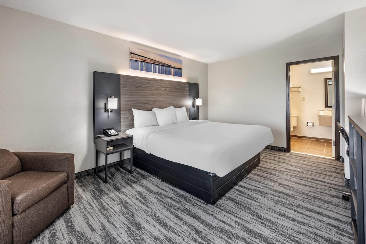 A hotel room with a large bed, a nightstand, a chair, and a wall-mounted TV.