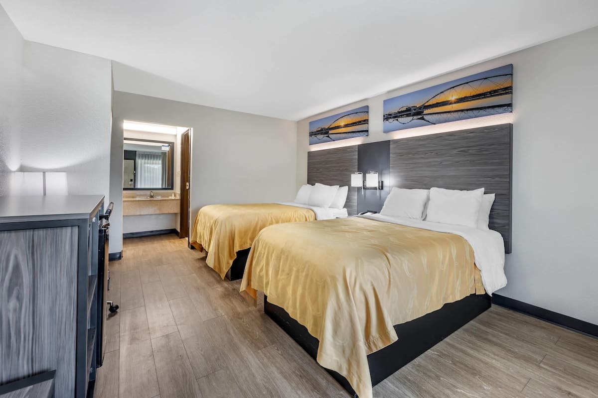 A hotel room with two beds, a desk, and a bathroom visible through an open door.