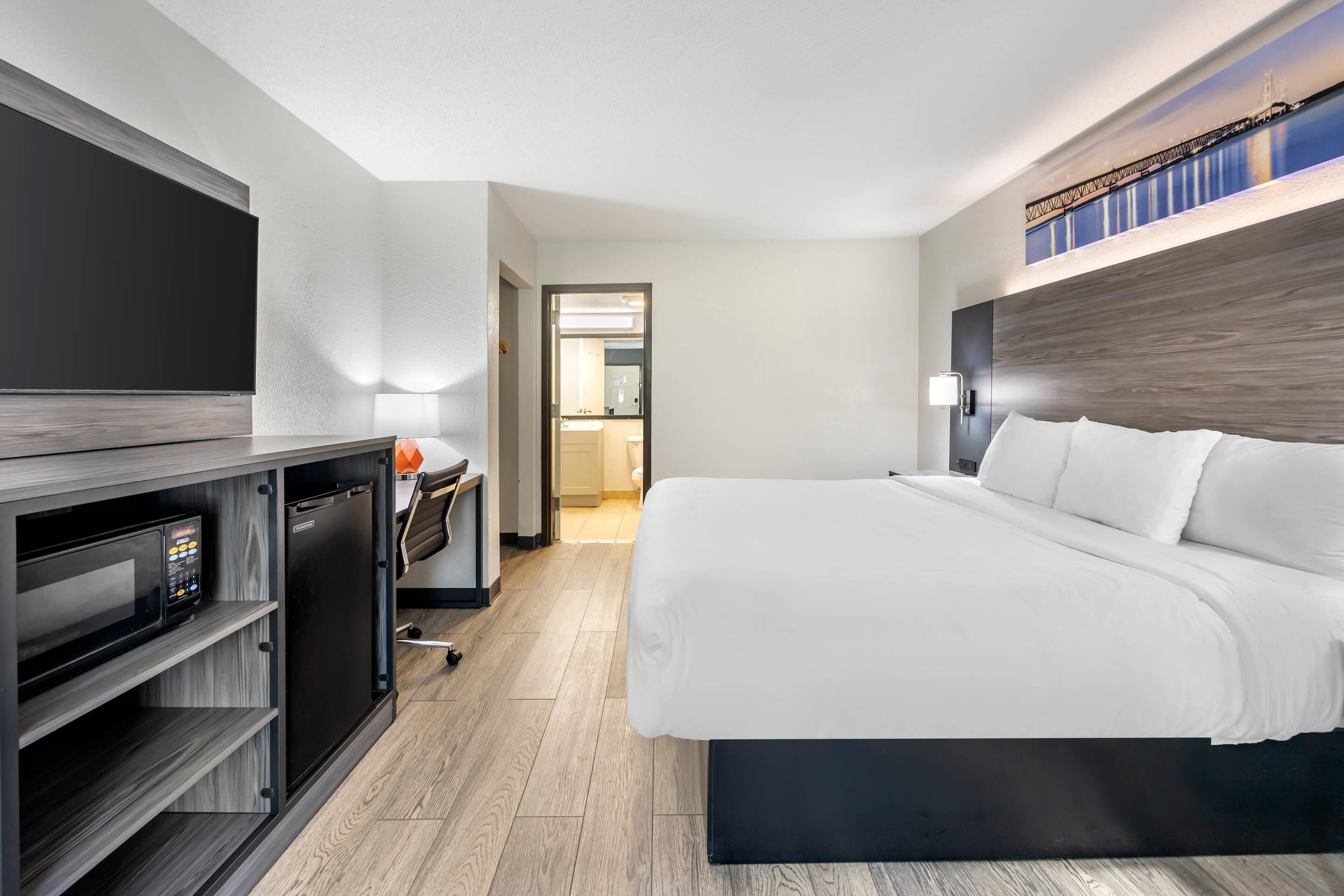 Ein modernes Hotelzimmer mit einem großen Bett, einem Schreibtisch mit Computer und einem Flachbildfernseher.