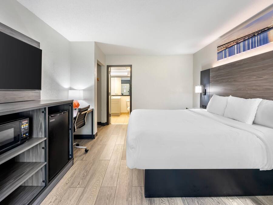 A modern hotel room with a large bed, a desk with a computer, and a flat-screen TV.