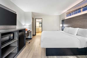 A modern hotel room with a large bed, a desk with a computer, and a flat-screen TV.