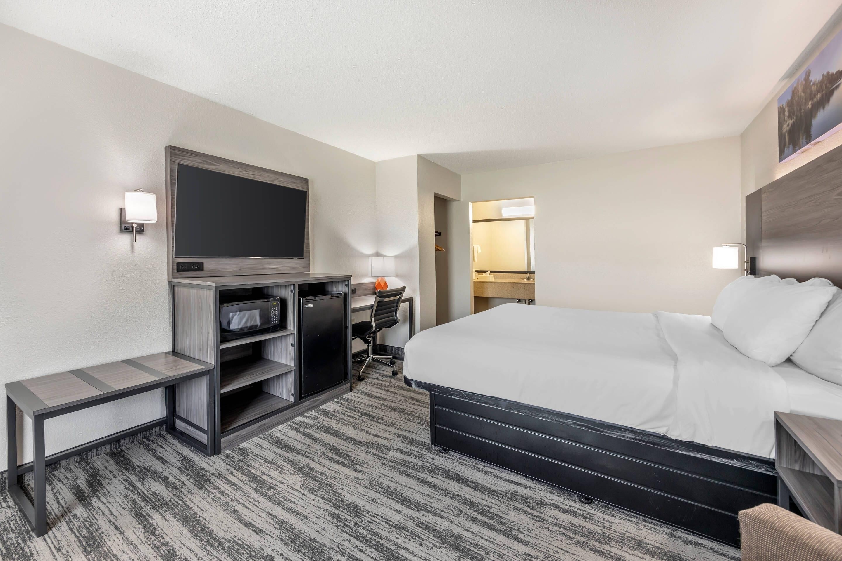 A hotel room with a large bed, a desk with a computer, a TV, and a small seating area.