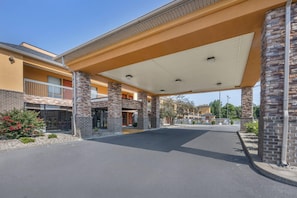 A hotel entrance with a covered walkway, stone pillars, and a clear sky.