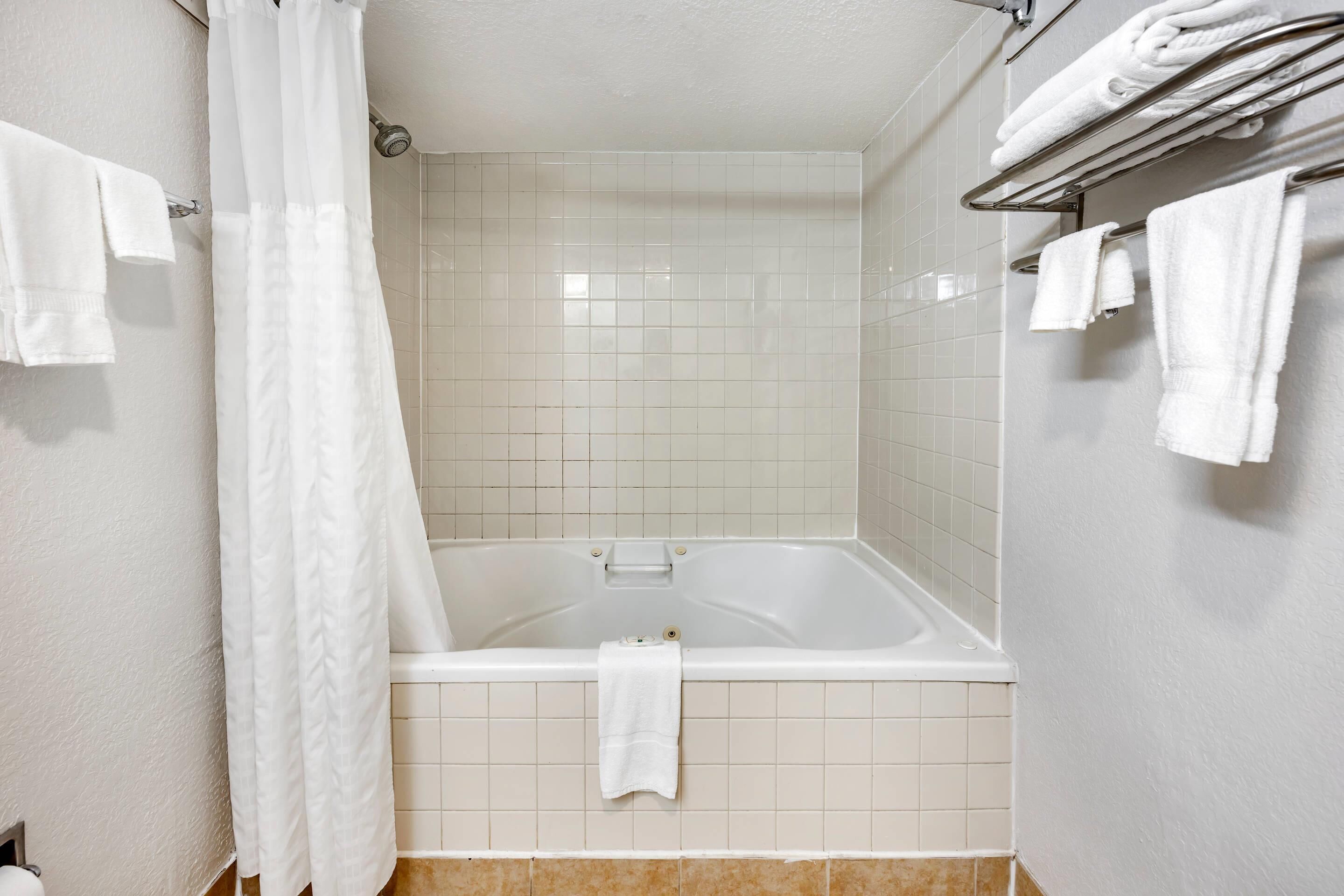 A bathroom with a bathtub, white tiles, and a towel rack with towels.