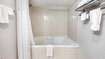 Un baño con bañera, azulejos blancos y un perchero con toallas.