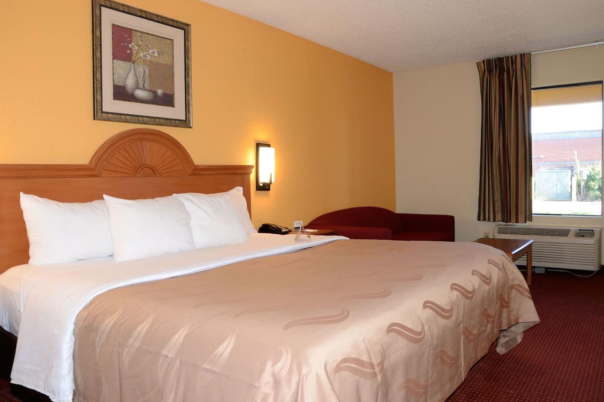 A hotel room with a large bed, a desk, a chair, a heater, and a window with curtains.