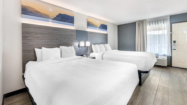A hotel room with two beds, a large window with curtains, a wall-mounted air conditioning unit, and two landscape paintings above the beds. - Quality Inn Glasgow (Glasgow)