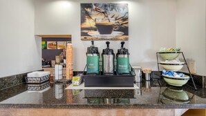 A coffee station with a coffee machine, hot water dispenser, and regular coffee dispenser. There are paper cups, a basket of napkins, and a tray of sugar packets. - Quality Inn Glasgow (Glasgow)