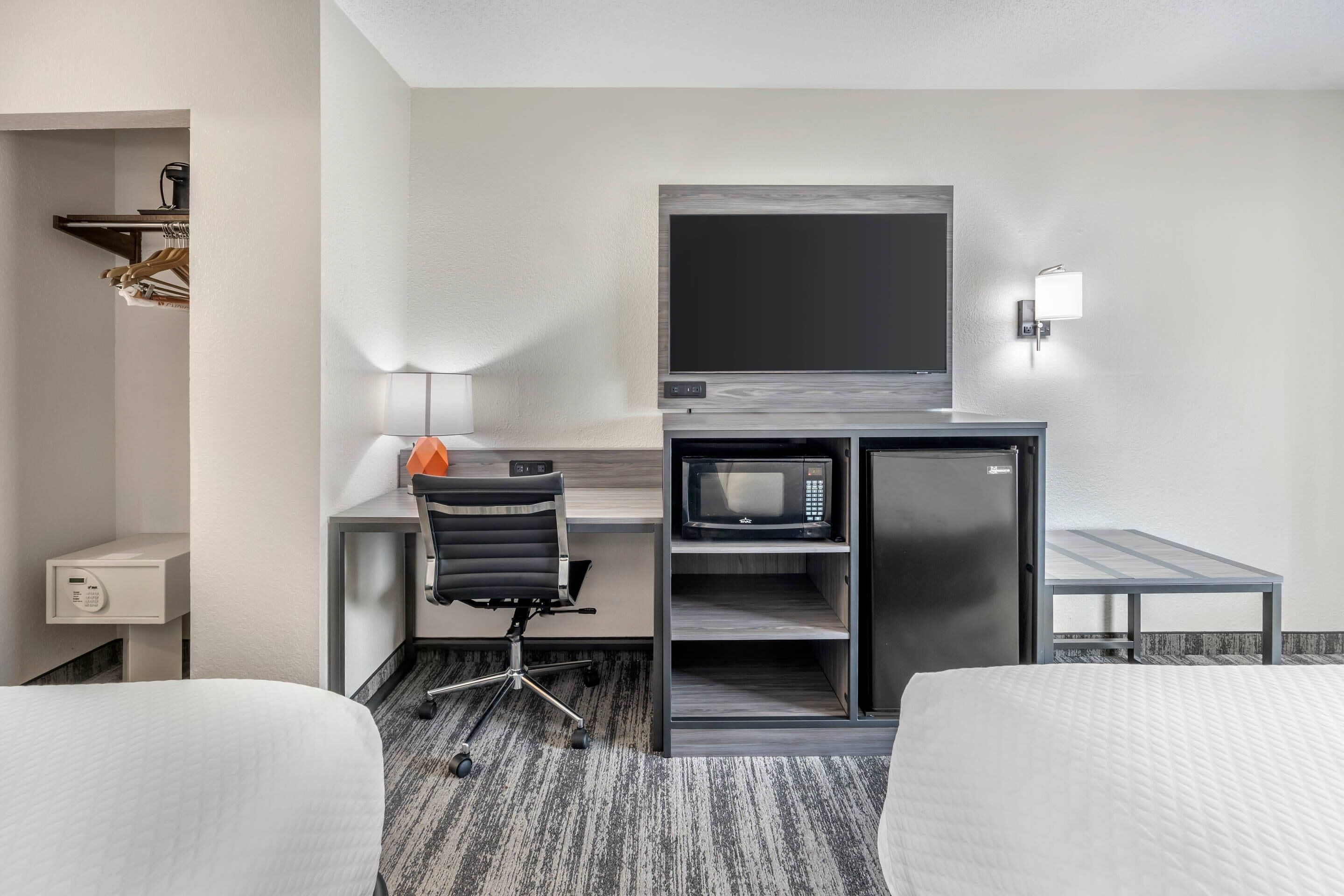 Une chambre d’hôtel comprenant un lit, un bureau avec une chaise, un four à micro-ondes, un réfrigérateur, une télévision et une table de chevet.
