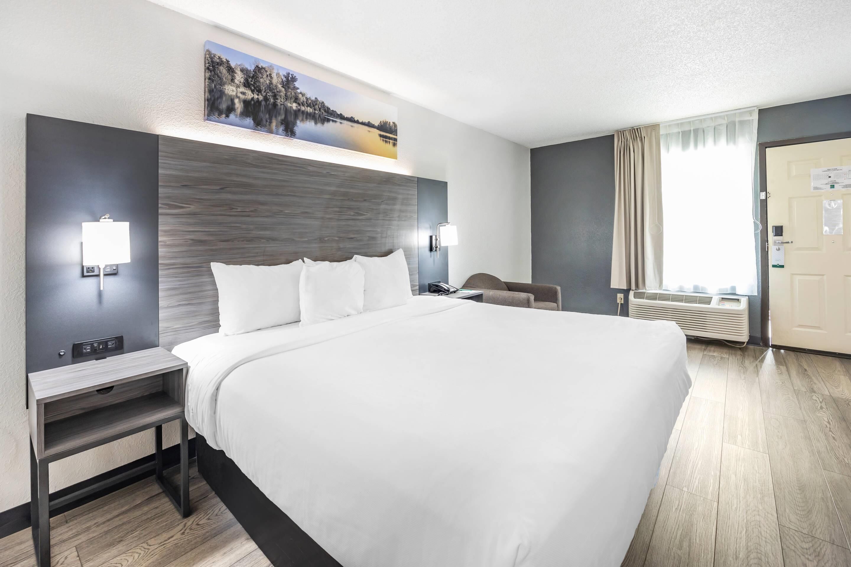 Ein modernes Hotelzimmer mit einem großen Bett, Nachttischen, einem Schreibtisch und einem Fenster mit Vorhängen.