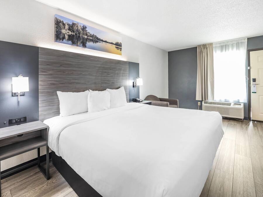 Ein modernes Hotelzimmer mit einem großen Bett, Nachttischen, einem Schreibtisch und einem Fenster mit Vorhängen.