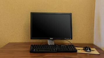 A Dell monitor, a black keyboard, and a mouse on a wooden desk against a beige wall.