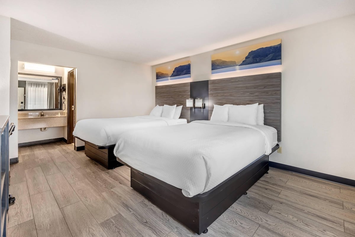 A hotel room with two beds, a bathroom with a mirror, and artwork on the wall.