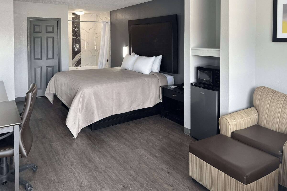 Ett modernt hotellrum med en stor säng, ett skrivbord, en stol, en soffa, en TV och en mikrovågsugn.
