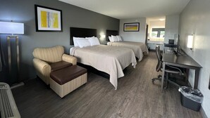 Quarto de hotel com duas camas, uma escrivaninha, uma cadeira, um abajur e uma lixeira.